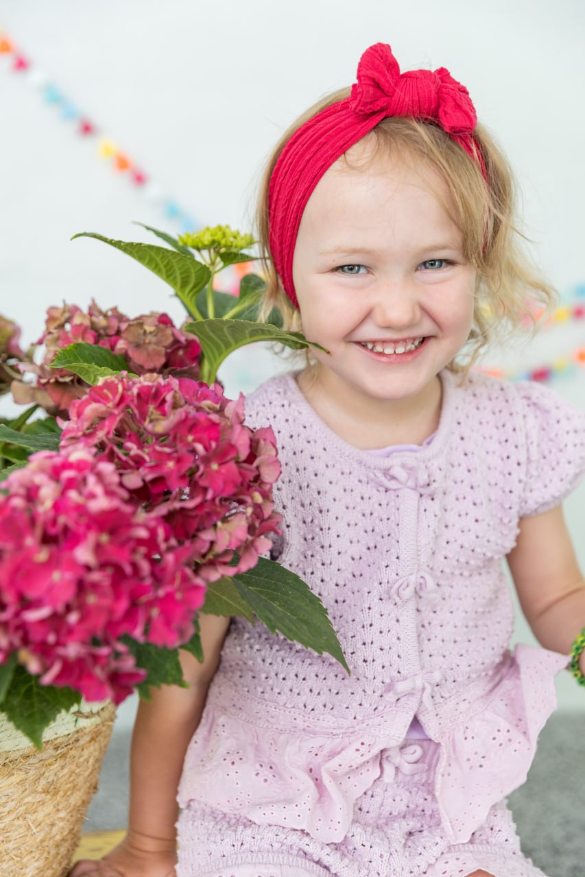 Lachendes Kindergartenkind mit rotem Haarband und Blumen