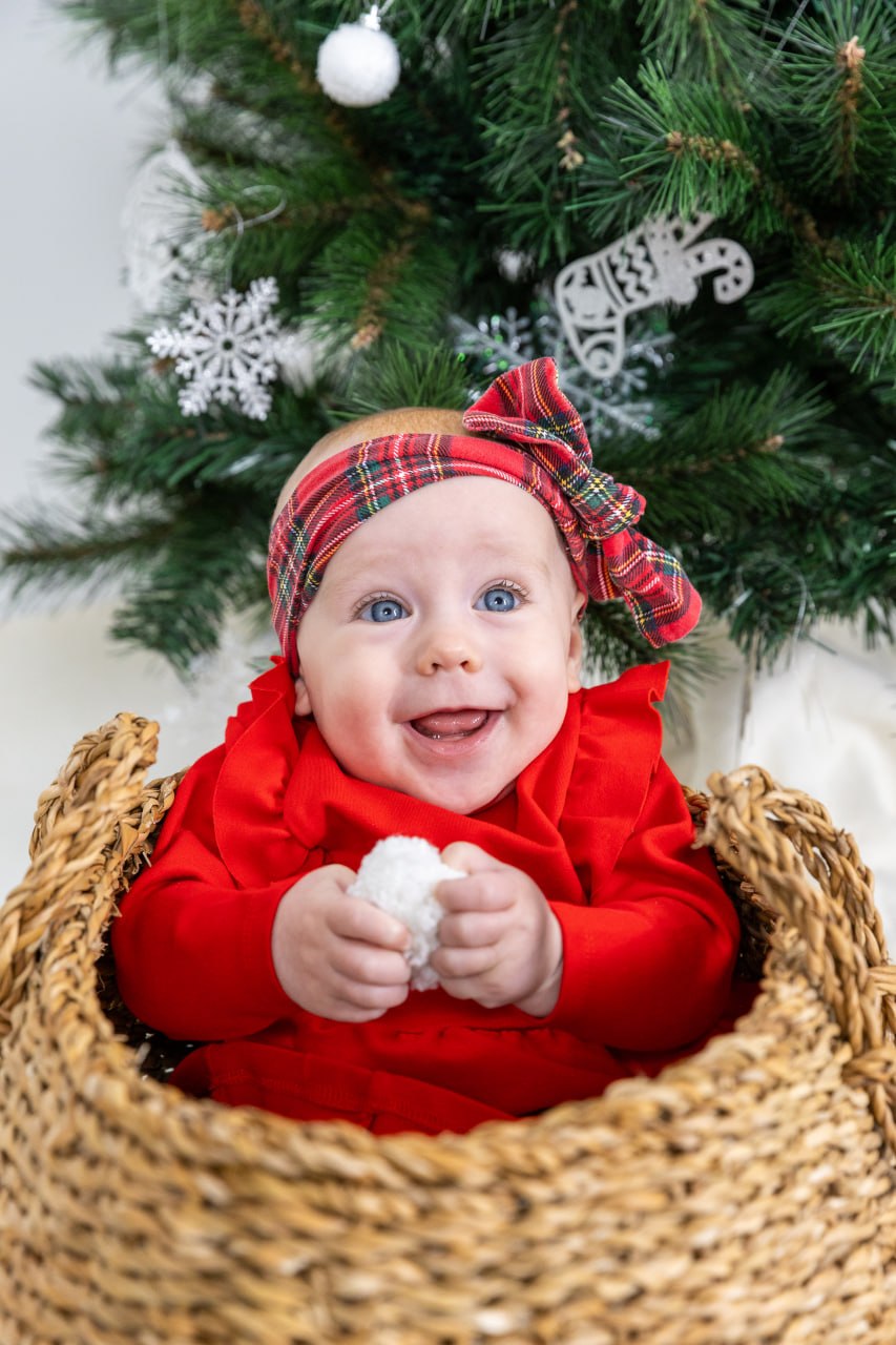 Lachendes Baby im roten Outfit vor einem Weihnachtsbaum